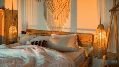 A boho bedroom with a white bedspread, wooden furniture and overhead lights
